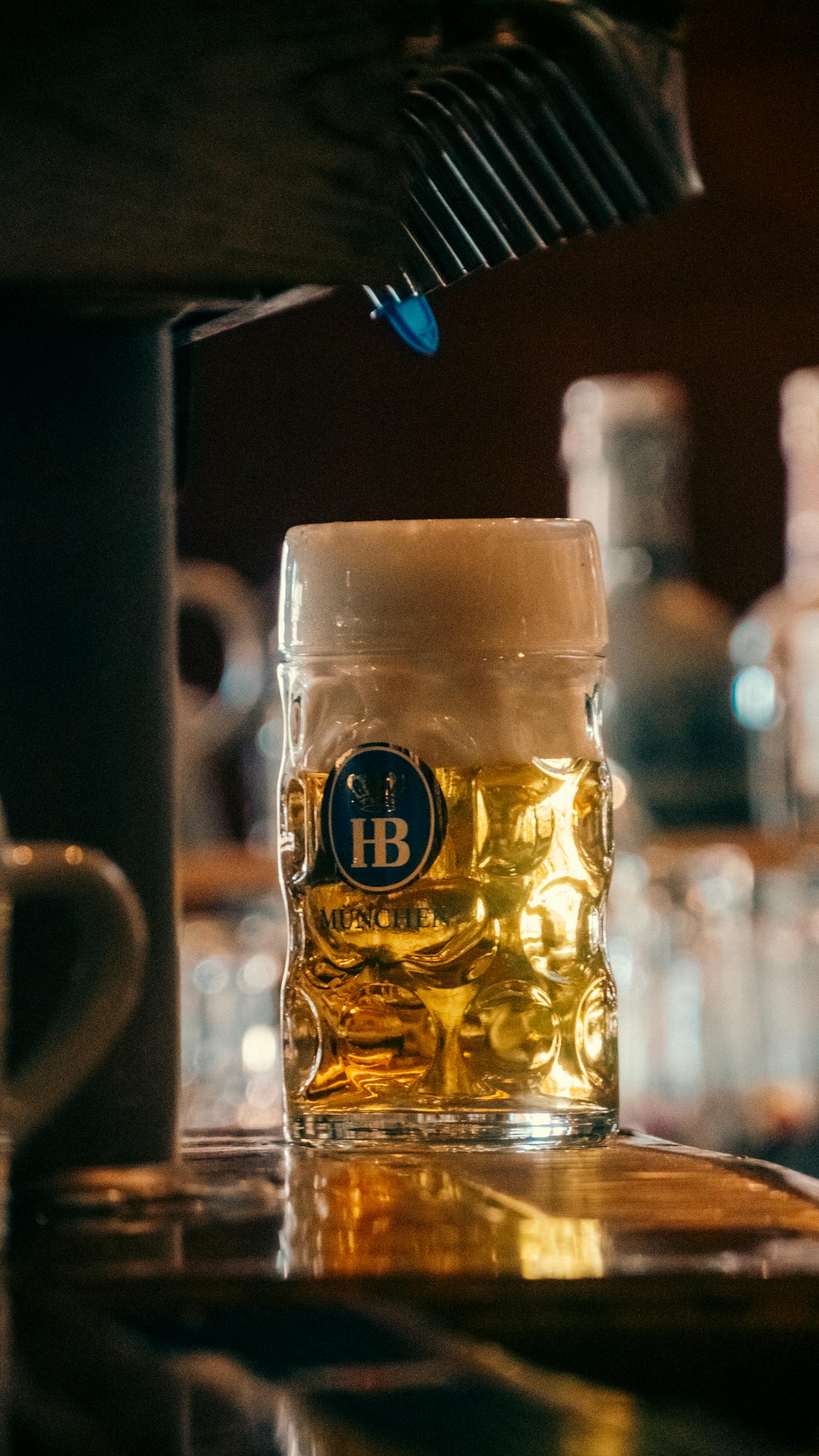 A glass of amber beer with frothy head on a dimly lit bar counter.